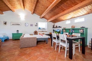 Una stanza accogliente con soffitto in legno, un letto, un tavolo da pranzo con sedie, un armadietto verde e una finestra.