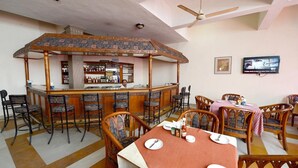 A bar area with a counter and stools, a dining area with tables and chairs, and a television mounted on the wall. - Blue Bird Hisar (Hisar)
