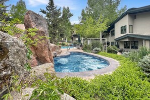 A swimming pool surrounded by rocks and greenery, with a house in the background.