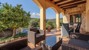 An outdoor patio area with wicker furniture, stone walls, and a view of the landscape.