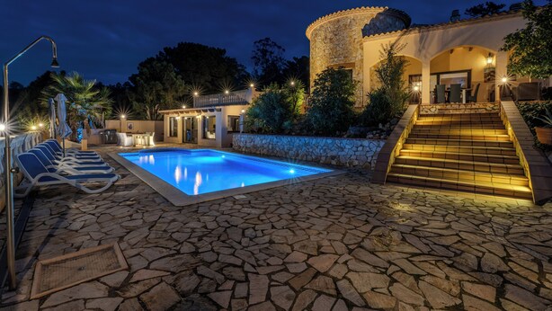 A stone-paved pool area with lounge chairs, a stone building with a dome, and a staircase leading to an upper level.