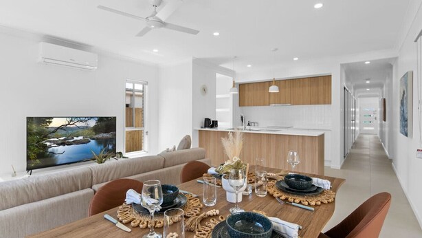 A modern dining area with a wooden table set for four, a sofa, and a television displaying a scenic landscape. - Secluded 4-Bed Retreat Mins to Beaches & Wineries (Victoria Point)
