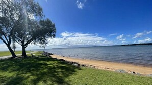 A beach with a grassy area, a pathway, and a large tree. - Secluded 4-Bed Retreat Mins to Beaches & Wineries (Victoria Point)