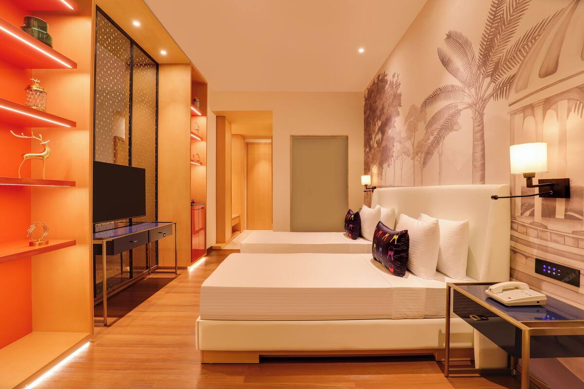 Ein Hotelzimmer mit Bett, Nachttisch, Fernseher und einer Wand mit Palmenmotiv.