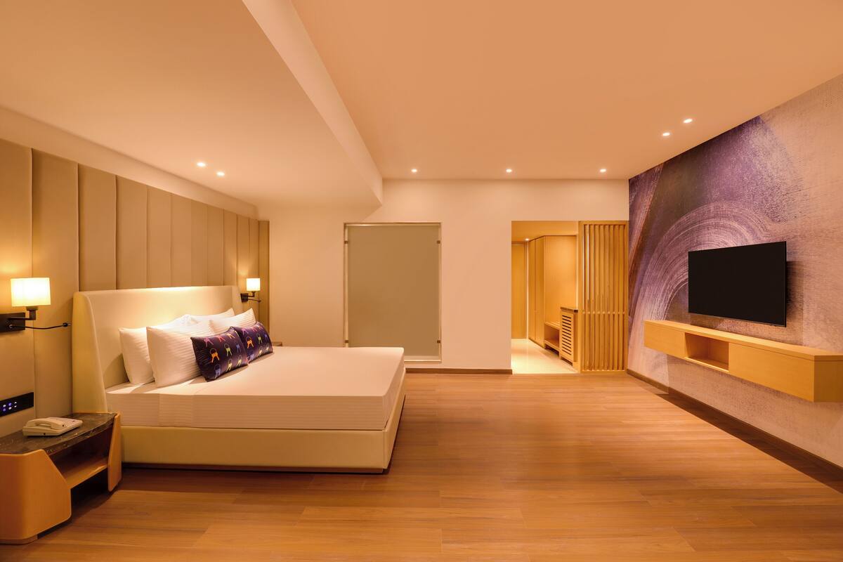 Ein modernes Hotelzimmer mit einem großen Bett, Nachttischlampen, einem flachbildfernseher an der Wand und Holzboden.