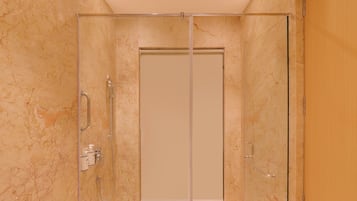 A glass-enclosed shower stall with a marble wall, a showerhead, and a handrail.