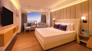 Een moderne hotelkamer met een groot bed, een televisie, een bank en uitzicht op de stad.