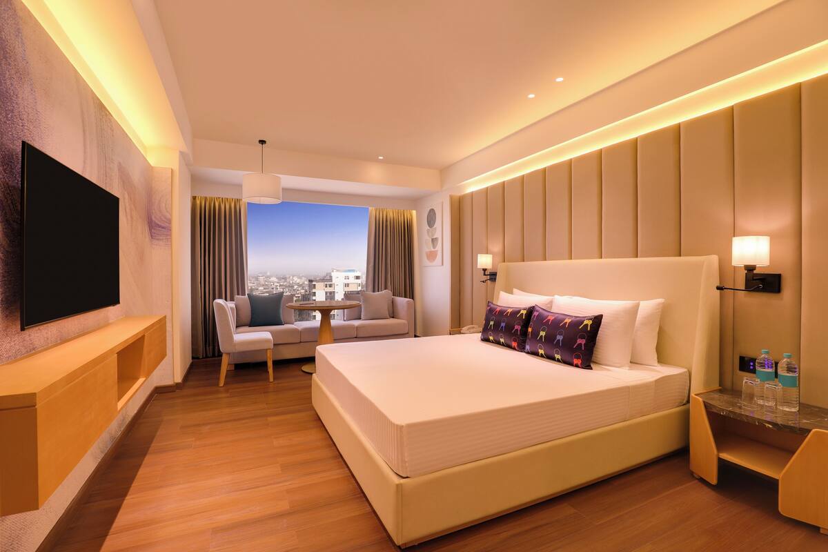 Ein modernes Hotelzimmer mit einem großen Bett, einem Fernseher, einer Couch und Blick auf die Stadt.