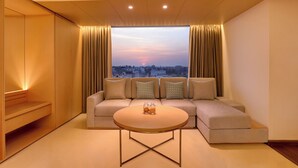Een moderne woonkamer met een bank, een salontafel en een uitzicht op een stadsgezicht bij zonsondergang.