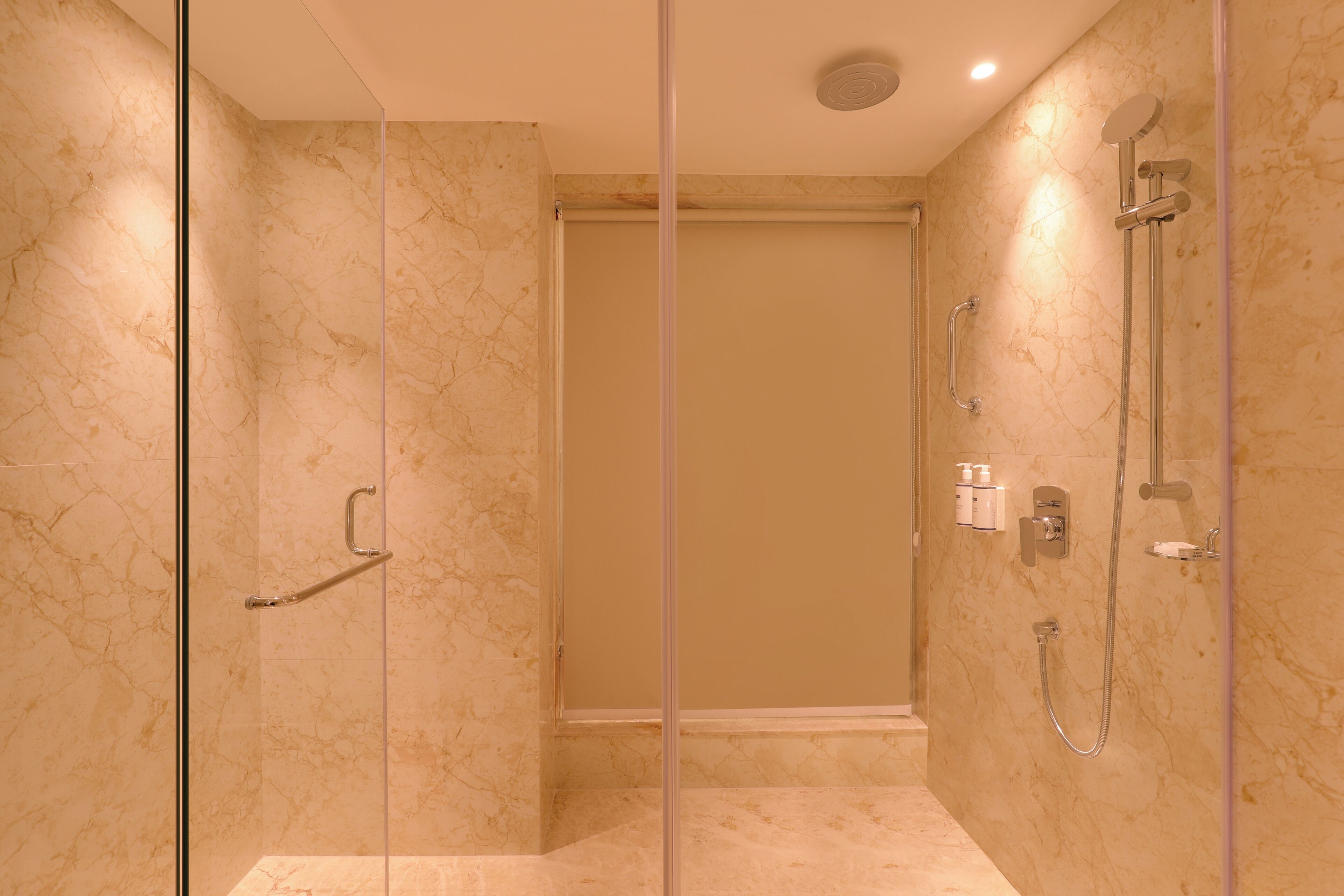 A modern bathroom with a glass shower enclosure, marble walls, and a handheld showerhead.