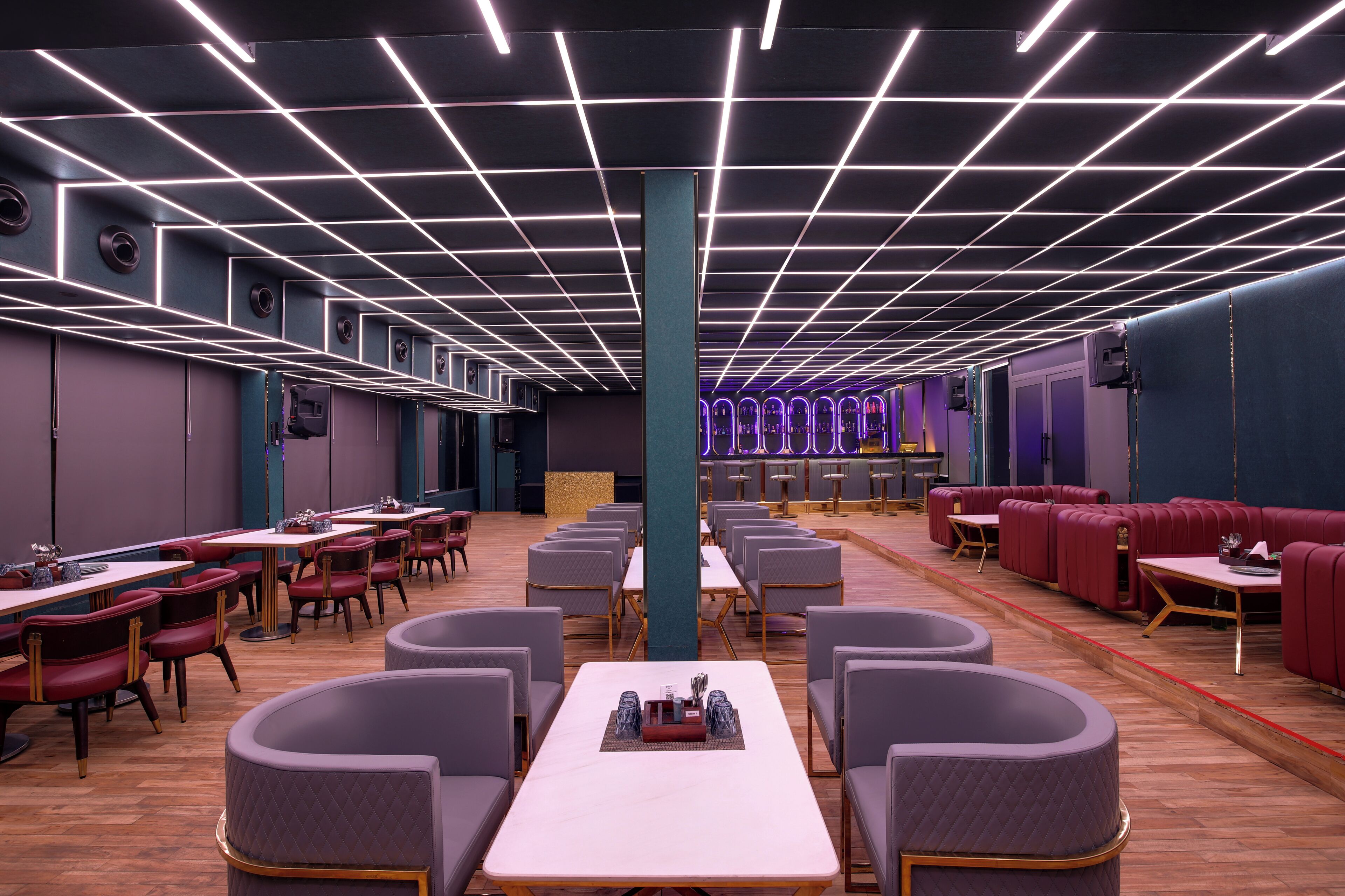 Un restaurante moderno con techo de diseño en cuadrícula, varias zonas de estar con mesas redondas y cabinas, y un pilar central.