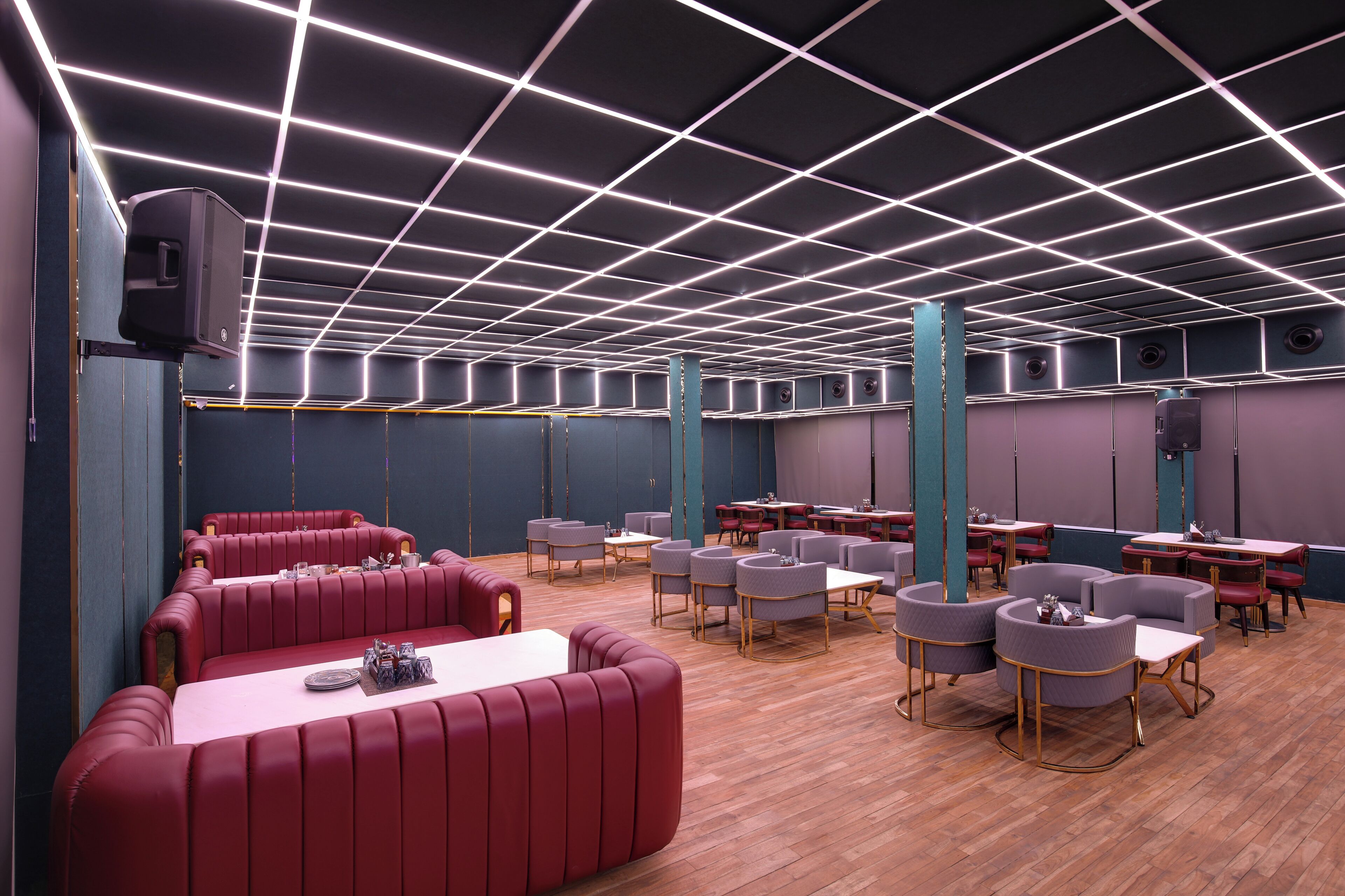 A modern restaurant with red booths, round tables, and a grid-patterned ceiling.