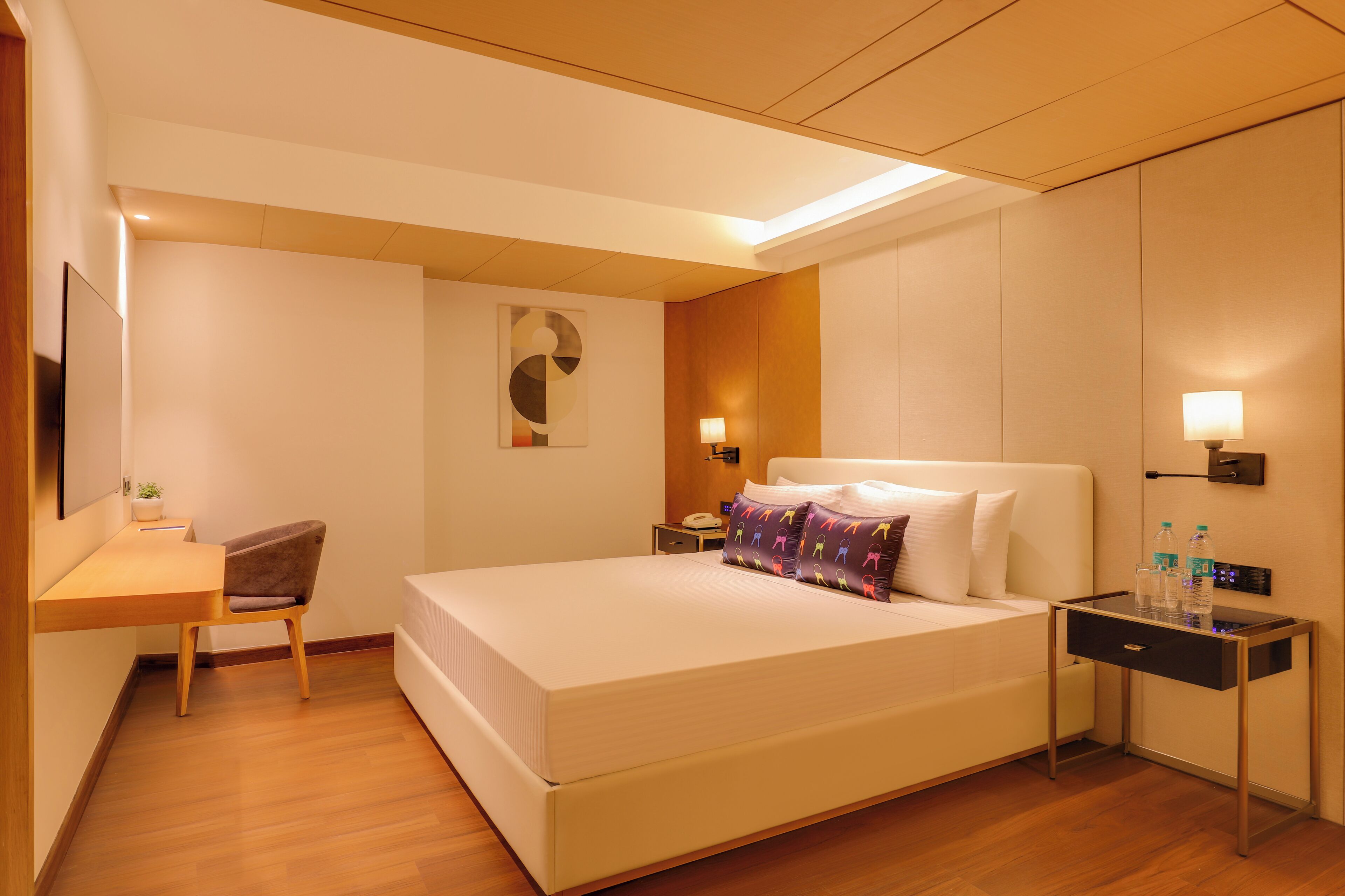 A hotel room with a bed, bedside table, desk, chair, and a wall-mounted TV.