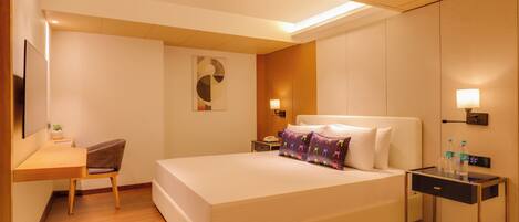 A hotel room with a bed, bedside table, desk, chair, and a wall-mounted TV.