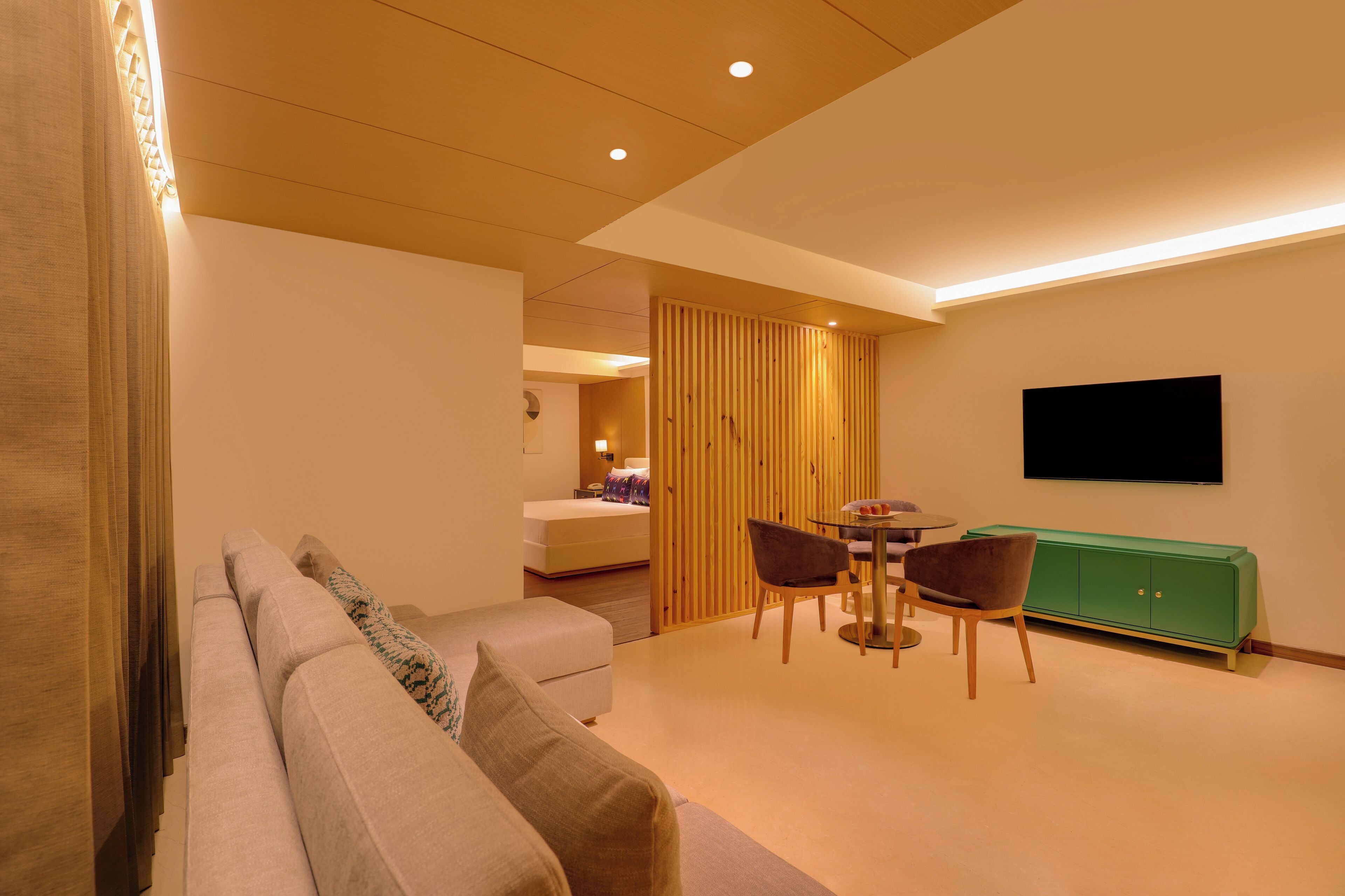 Un salon moderne comprenant un canapé, une table à manger avec des chaises, un meuble vert et un téléviseur à écran plat fixé au mur.