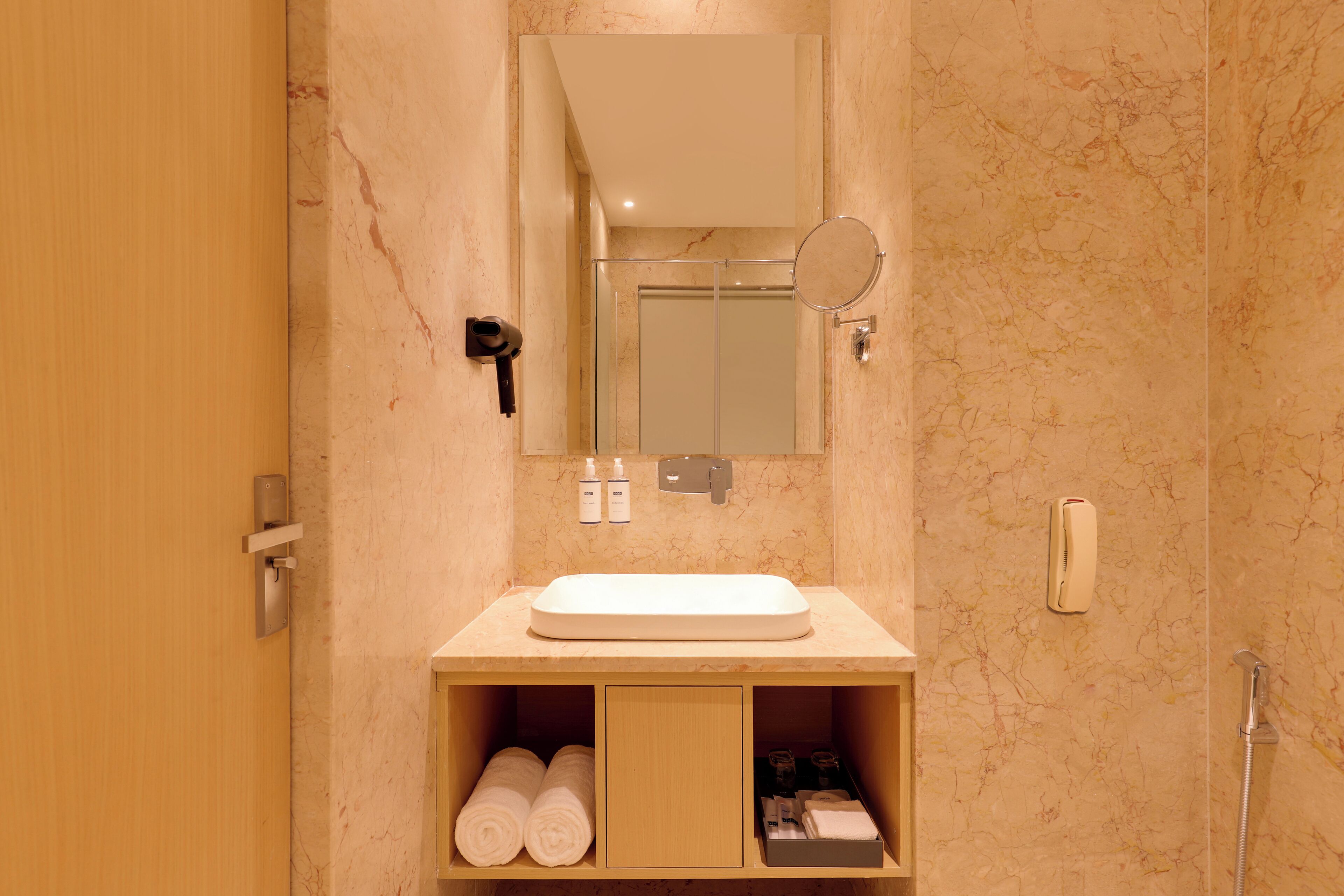 Un baño con pared de mármol, un lavamanos, un espejo, un perchero para toallas y una ducha.