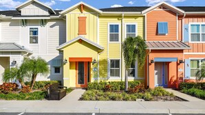A row of colorful townhouses with distinct architectural styles, each featuring a front porch and a small garden area.