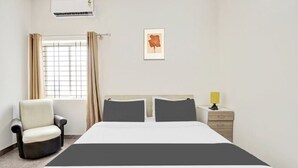 A hotel room with a bed, a chair, a bedside table with a lamp, a window with curtains, and a framed picture on the wall. - Welcome Inn Express (Bengaluru)