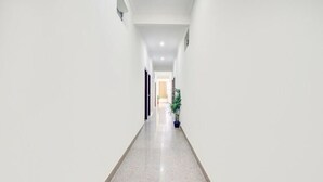 A long, narrow hallway with white walls and a polished floor, leading to a door at the end. - Welcome Inn Express (Bengaluru)