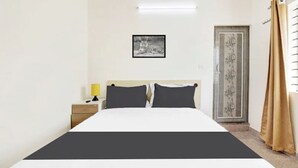 A bedroom with a bed, bedside table, lamp, framed artwork, and a door with decorative paneling. - Welcome Inn Express (Bengaluru)
