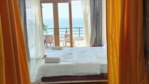 A room with a bed, a view of the sea, and a balcony with chairs. - Vivaans Beach Resort (Canacona)