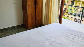 A room with a bed, wooden wardrobe, and a view of a balcony with palm trees.