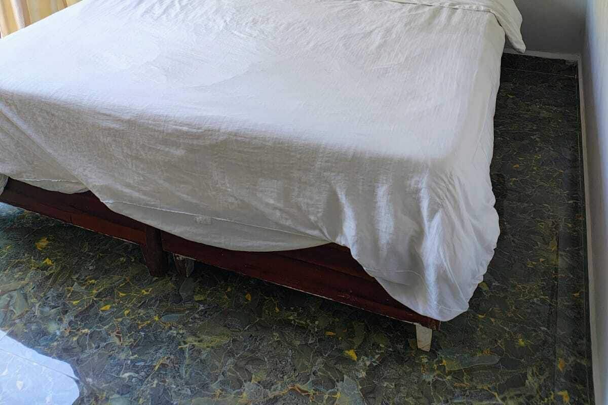 A single bed with white bedding in a room with plain walls and a tiled floor.