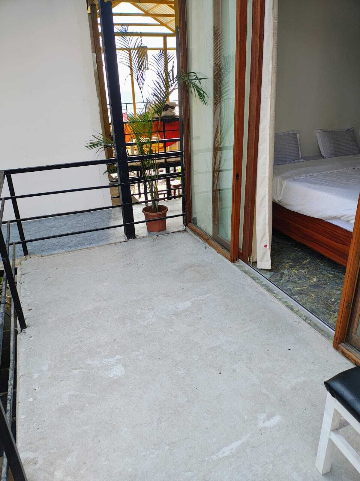 Un balcón con piso de concreto, una planta en maceta y una cama con ropa blanca.