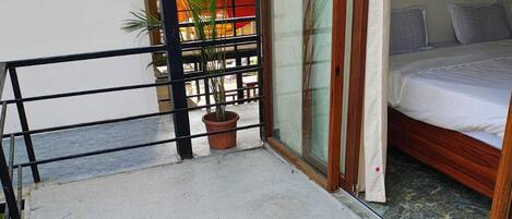 Un balcón con piso de concreto, una planta en maceta y una cama con ropa blanca.