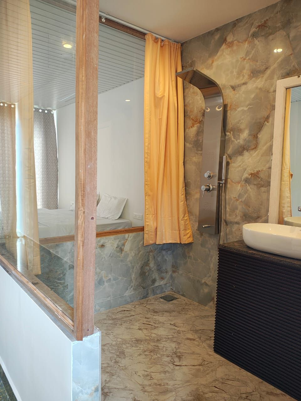 A modern bathroom with a marble floor, a shower with a glass door, and a wooden vanity with a sink.