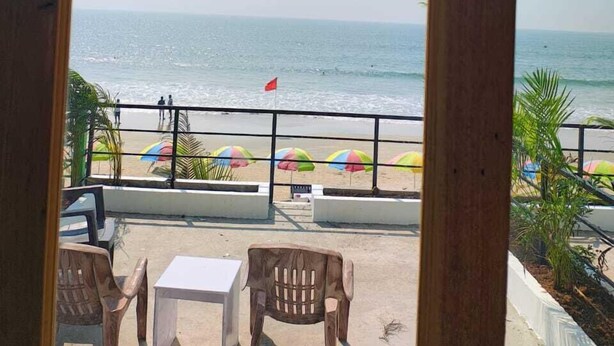 A view from a balcony overlooking a beach with a flag, umbrellas, and a table with chairs. - Vivaans Beach Resort (Canacona)