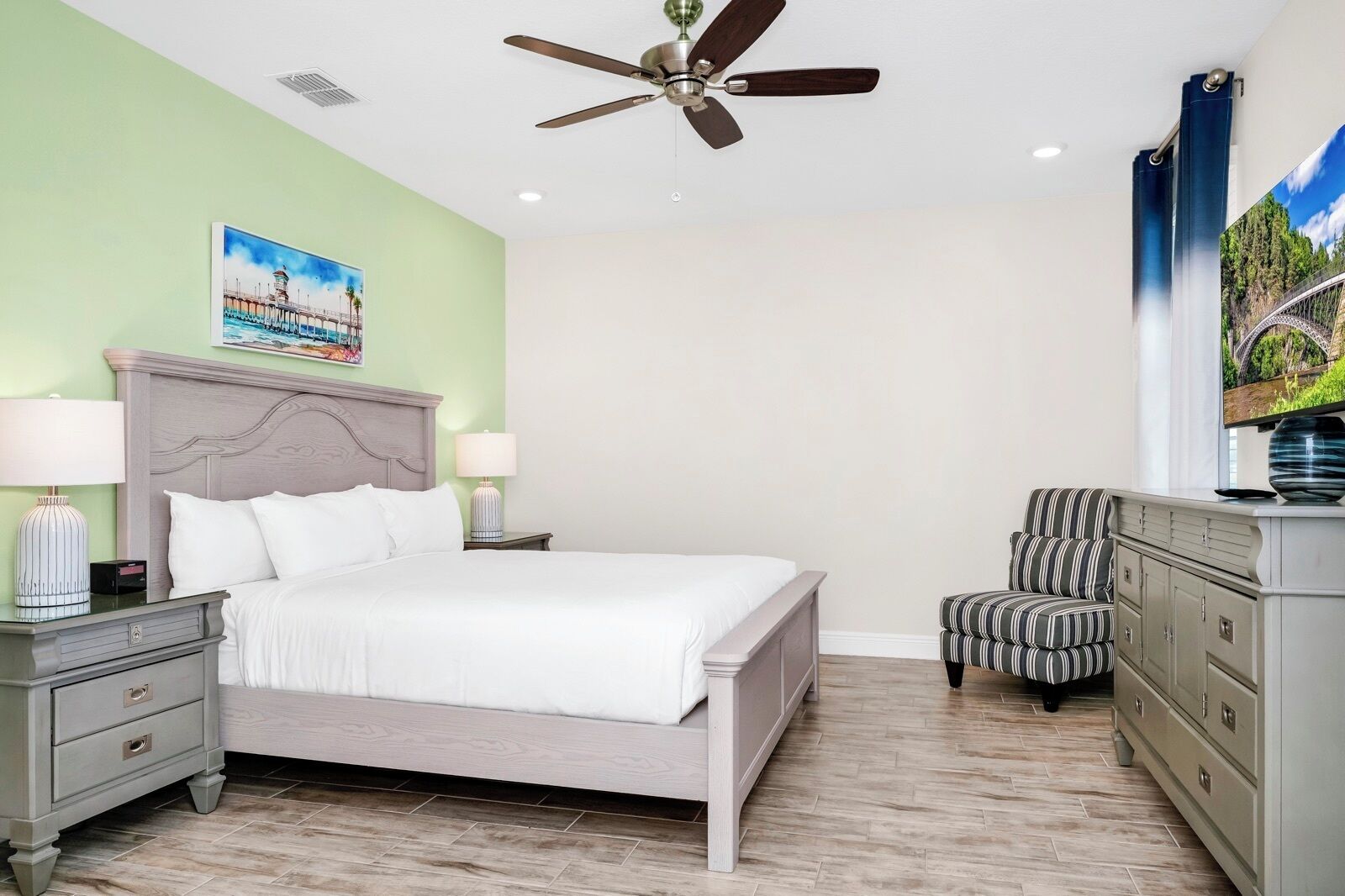 A bedroom with a bed, nightstands, a dresser, a chair, a ceiling fan, and a painting on the wall.