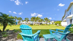 Un espace patio avec deux fauteuils Adirondack turquoise, donnant sur une pelouse bien entretenue et une rangée de bâtiments en arrière-plan.