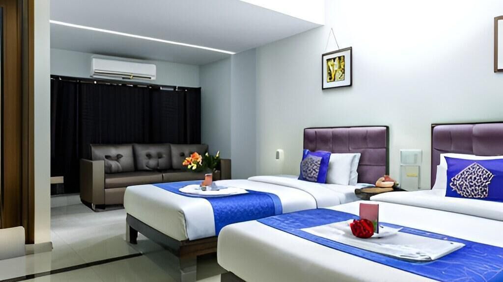 A hotel room with two beds, a sofa, an air conditioning unit, and a framed picture on the wall.