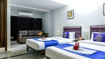 A hotel room with two beds, a sofa, an air conditioning unit, and a framed picture on the wall.
