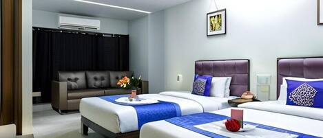 A hotel room with two beds, a sofa, an air conditioning unit, and a framed picture on the wall.