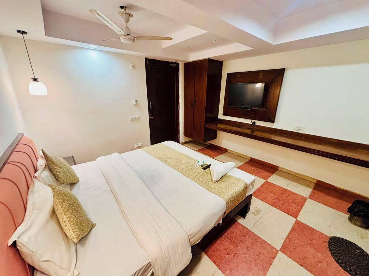 Una habitación de hotel con cama, televisor, ventilador de techo y piso a cuadros.