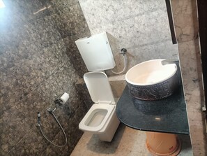 A bathroom with a toilet, bidet, and a sink with a decorative basin. - Hotel Seven Inn (Ahmedabad)