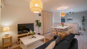 A modern living room with a TV, sofa, coffee table, and dining area. - Seiwa Travel Time Sunahama (Osaka)