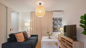 A modern living room with a dark sofa, a white coffee table, a TV on a wooden stand, and a large window with curtains. - Seiwa Travel Time Sunahama (Osaka)