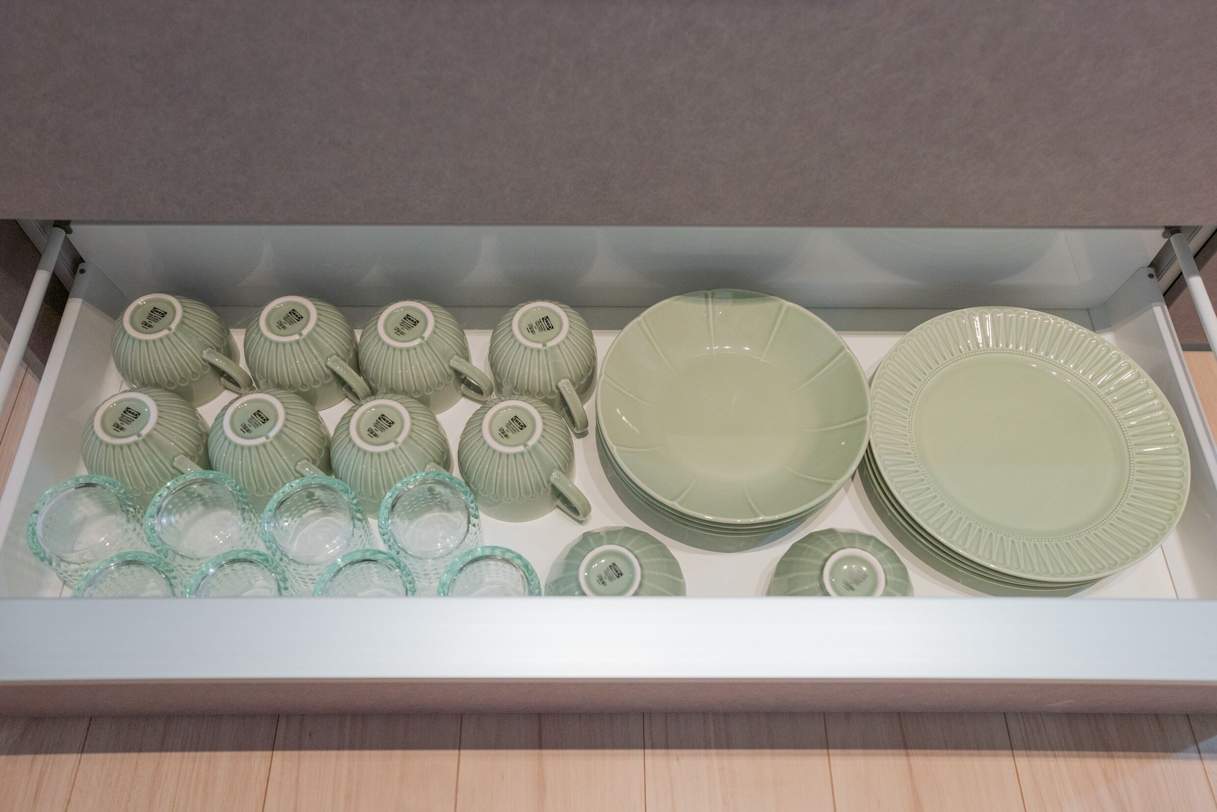 A drawer containing various green ceramic dishes, including plates, bowls, and cups.