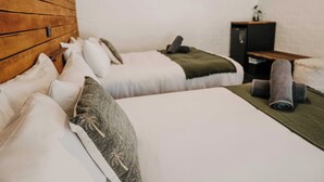 A hotel room with two single beds, a wooden headboard, a small desk with a computer, and a green blanket on one bed.