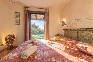 A hotel room with a bed, a breakfast tray, a vase with flowers, and a view of the outdoors. - Villa Sul Golfo (Arzachena)