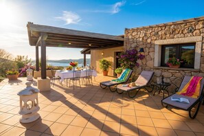 A terrace with a table and chairs, lounge chairs, and potted plants. - Villa Sul Golfo (Arzachena)