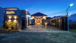 A hotel entrance with a checkered pathway leading to a wooden door, illuminated by ground lights and a neon sign. - Luxury 5-bedroom villa in beautiful West Java with AC, WiFi, Private Pool (West Java)