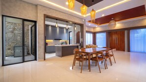 A modern kitchen with a central island, a dining area with a wooden table and chairs, and a large window with curtains. - Luxury 5-bedroom villa in beautiful West Java with AC, WiFi, Private Pool (West Java)