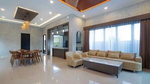 A spacious living room with a modern sofa, a dining table with chairs, and a kitchen area in the background. - Luxury 5-bedroom villa in beautiful West Java with AC, WiFi, Private Pool (West Java)