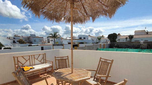 Una terraza en la azotea con una mesa y sillas, un parasol de paja y vistas al vecindario.