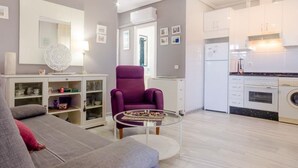 A modern apartment with a grey sofa, a purple armchair, a glass coffee table, a kitchen with white cabinets, and a white refrigerator. - Pinar 12 14334 in Chiclana (Chiclana de la Frontera)