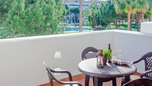A balcony with a round table, two chairs, a potted plant, a lantern, and a glass of wine.